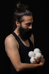 Bearded man with balls standing against black background