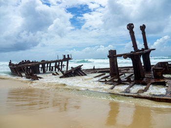 Wooden posts on beach against sky