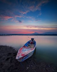 Boat moored on beach against sky during sunset