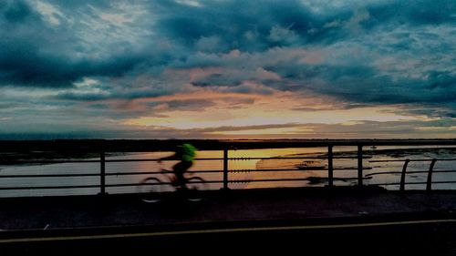 Silhouette man by sea against sky during sunset