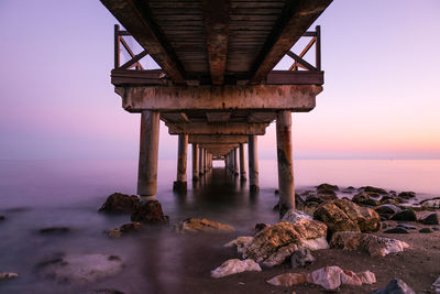 Below view of jetty in sea against sky during sunset