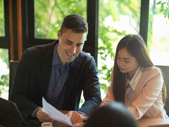 Young couple looking away while sitting on window