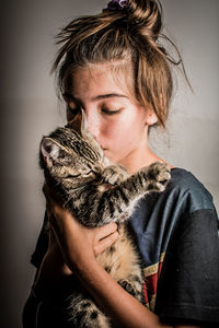 Close-up of cute girl holding cat standing against wall at home