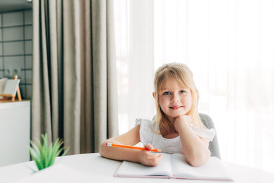 Portrait of smiling girl sitting on table at home