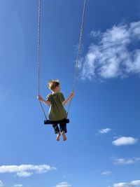 Low angle view of boy swinging against sky