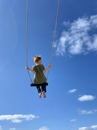 Low angle view of man swinging against sky