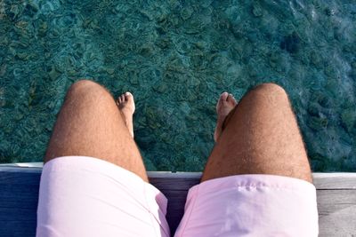 Low section of man sitting on pier over sea