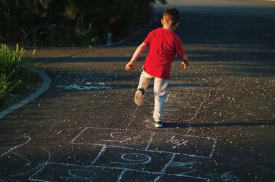 Rear view of boy playing hopscotch on footpath