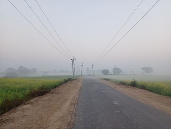 Road amidst field against sky during foggy weather