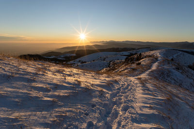 Snow covered landscape against sky during sunset