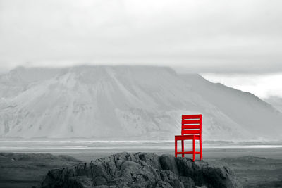 Red chair on rocky hill with scenic view of mountains in background during cloudy afternoon