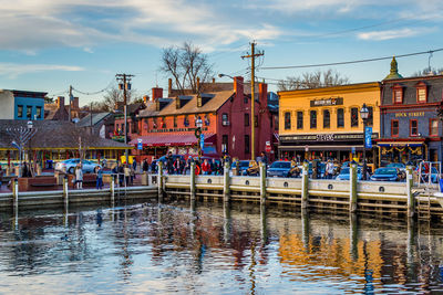 People in canal by buildings against sky in city