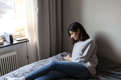 Young woman lying on bed and using smart phone