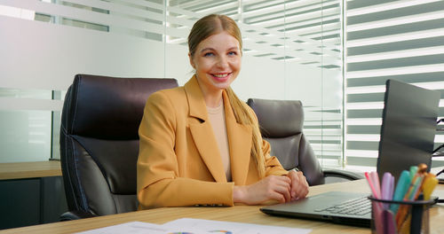 Portrait of business woman looking in camera and working on laptop in office. 