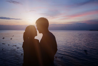 Woman standing by sea against sky during sunset