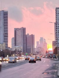 Vehicles on road against buildings at sunset