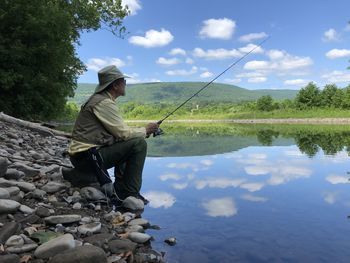 Man sitting on rock by lake against sky