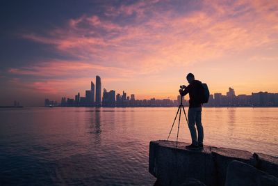 Rear view of silhouette man standing in sea against sky during sunset