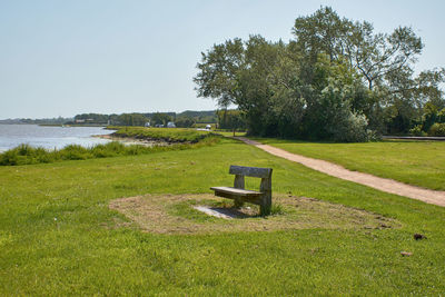 Empty bench on field by trees against sky