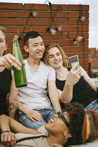 Smiling men sharing mobile phone by female friends on rooftop