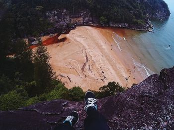 Low section of person sitting on rock against beach