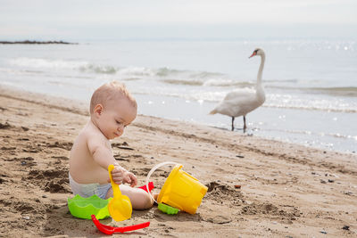 Shirtless baby boy playing with toys at beach