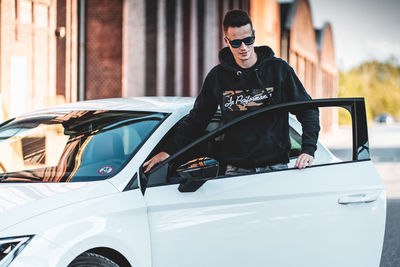 Portrait of man wearing sunglasses standing against car