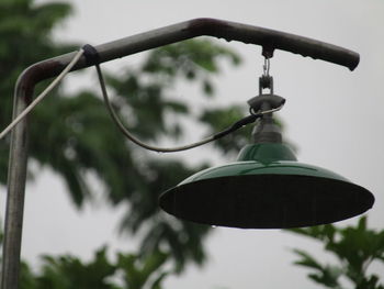 Low angle view of electric lamp hanging on street against sky