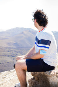 Side view of woman sitting on rock against mountain