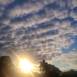 Low angle view of sunlight streaming through clouds during sunset