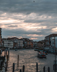 Sailboats in canal by city buildings against sky at sunset