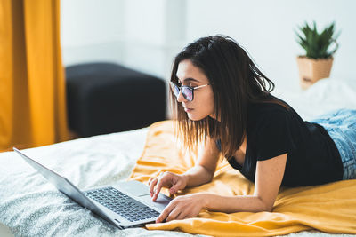 Female lying in bed at home using laptop touchpad. freelance lifestyle and work from home concept.