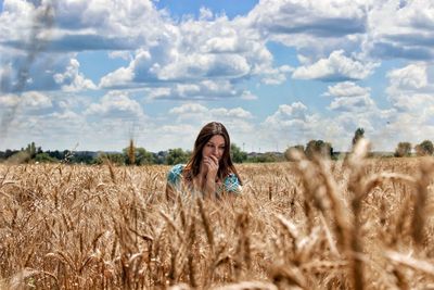 Woman looking away while sitting amidst plants against sky