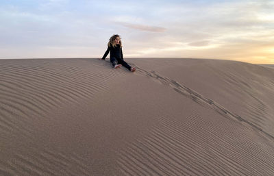 A child sits atop a sand dune at great sand dunes national park and preserve in colorado