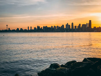 Sea by buildings against sky during sunset