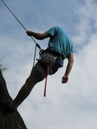 Low angle view of man climbing rock against sky