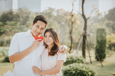 Portrait of smiling young couple standing against trees