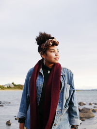 Portrait of young woman standing at beach against sky