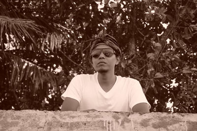 Portrait of young man looking away against trees