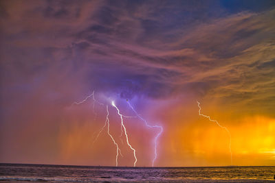 Lightning over sea against sky during sunset