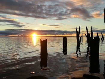 Silhouette wooden posts in sea against sky during sunset