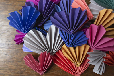 Multi-colored homemade paper origami hearts layered on wooden desk