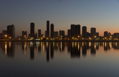 Reflection of illuminated city skyline on river against clear sky at dusk