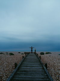 Man standing on pier at beach against sky