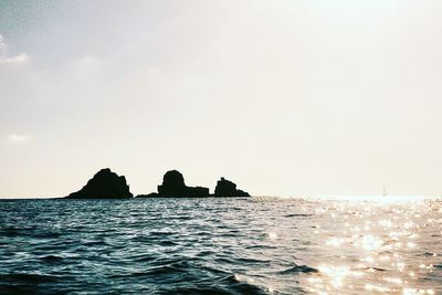 Silhouette rocks on sea against clear sky