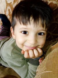Close-up portrait of cute smiling boy with hand on chin lying on sofa at home