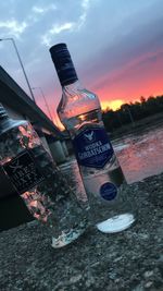 Close-up of beer bottle against sea during sunset