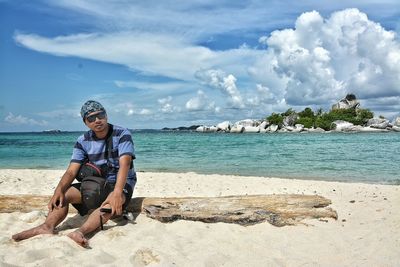 Full length portrait of man sitting on wood at beach