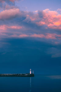 Lighthouse amidst sea and buildings against sky