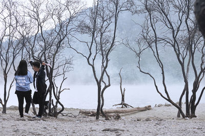 Friends at lakeshore against bare trees